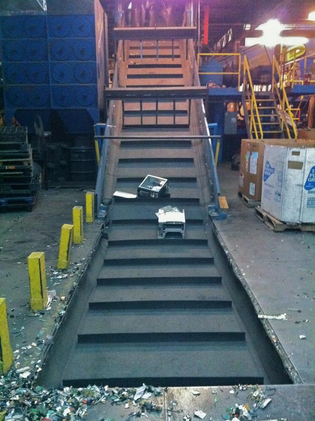 The Gateway computer, along with a medium-sized printer, rides a conveyor belt leading into a large shredder.