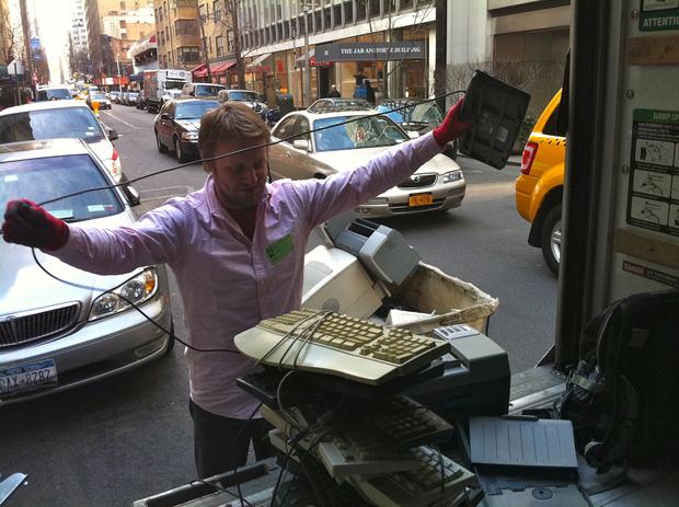 Kirsch detangles the chord of an old keyboard before stacking it on top of other e-waste items for weighing.