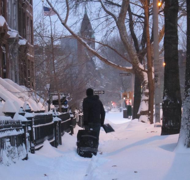 A man tows his suitcase along 6th Avenue in Brookly, carrying a snow shovel just in case.