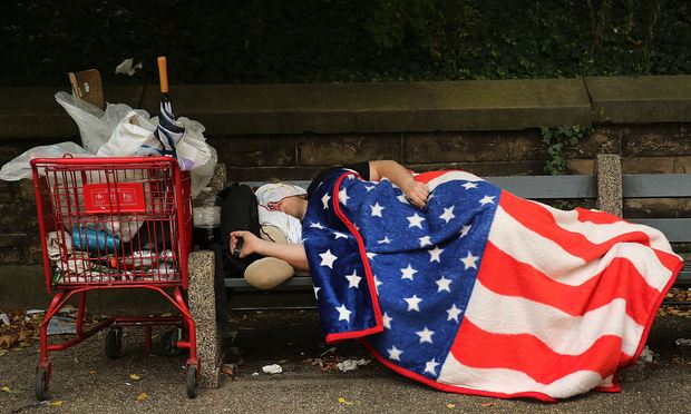 A homeless man sleeps under an American Flag blanket on a park bench on September 10, 2013 in New York City