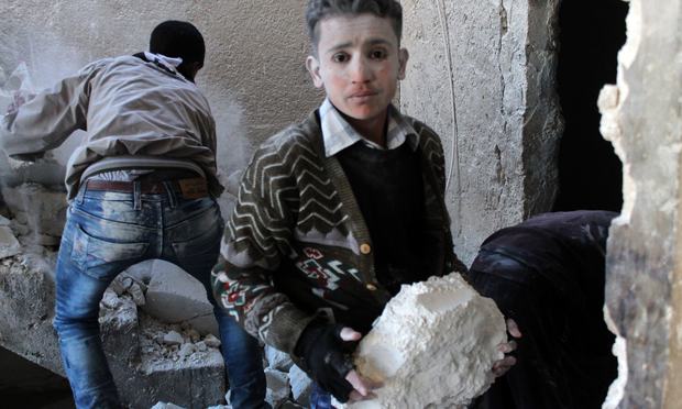 A young Syrian, covered is dust, helps clear the debris after the Syrian airforce allegedly fired at a residential neighborhood. December 9, 2013
