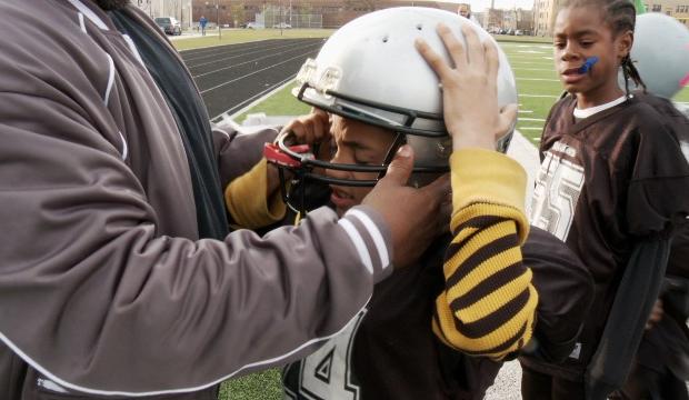 A young football player adjusts his helmet before a game in a scene from Steve James’ “Head Games”