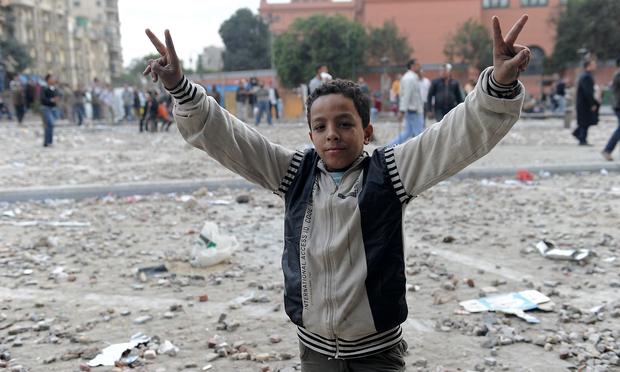 A young Egyptian anti-government demonstrator flashes victory signs as a stone battle rages between fellow demonstrators and pro-regime opponents at Cairo's Tahrir Square