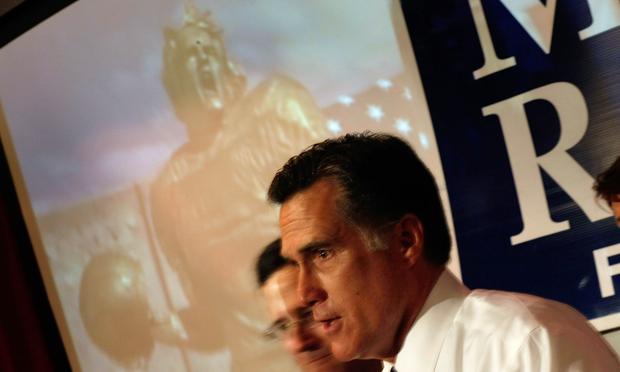 Republican presidential candidate and former Massachusetts Gov. Mitt Romney speaks to the media as a television ad plays behind him.