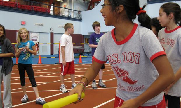 Relay racing is one of three activities 5th graders at PS107 participate in during gym class A girl lines up to run carrying a baton wearing a PS107 tshirt