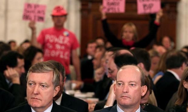 Lamar McKay (R), president and chairman of BP America Inc, and David Nagel (L), Executive Vice President of BP America,wait to testify as people protest behind them during a Senate hearing.