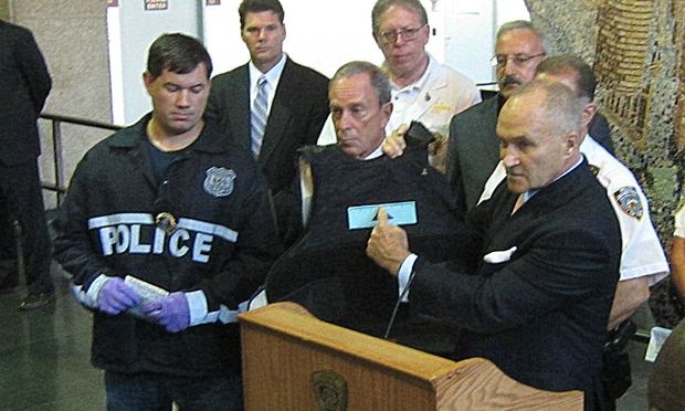 Police Commissioner Ray Kelly, flanked by Mayor Michael Bloomberg, holds up the shot officer's bullet-proof vest.