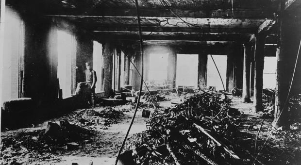 An officer stands at the Asch Building’s 9th floor window after the Triangle fire. Sewing machines, drive shafts, and other wreckage of the Triangle factory fire are piled in the center of the blaze-s