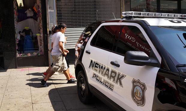 People walk by a police car in downtown on May 13, 2014 in Newark, New Jersey.