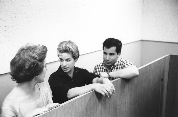 CIRCA 1959: Singer songwriters Carole King (center) and Paul Simon talk between takes in a New York, New York recording studio, circa 1959.