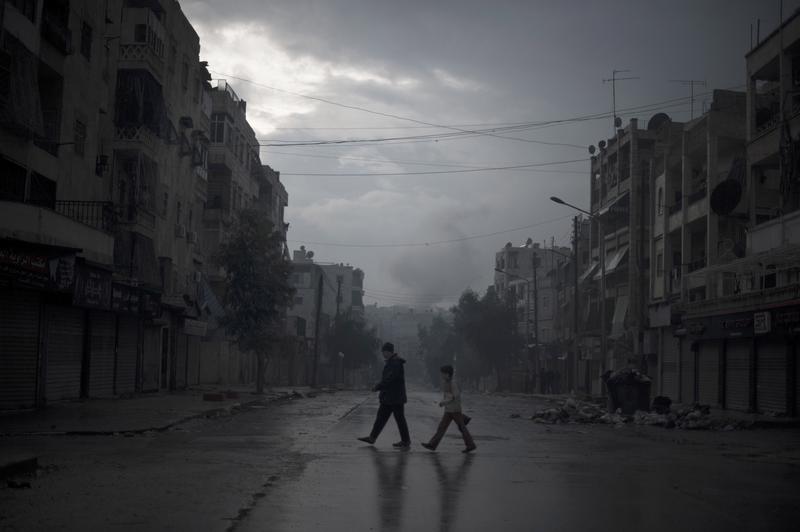 A father and son return home with vegetables, as smoke from a pro-government forces artillery strike ascends in the background, in the al-Amaria neighborhood in the city of Aleppo, on January 6, 2013.