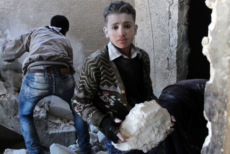 A young Syrian, covered is dust, helps clear the debris after the Syrian airforce allegedly fired at a residential neighborhood. December 9, 2013