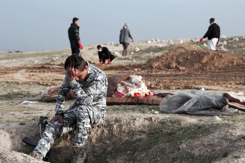 An Iraqi policeman collects himself as he is surrounded by bodies at the site of a mass grave containing some two dozen people, many of them children, in an area recently re-taken from ISIS. 3.14.17