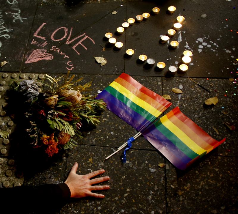 A man touches the ground next to rainbow flags during a candlelight vigil for the victims of the Pulse Nightclub shooting in Orlando, Florida on June 13, 2016 in Sydney, Australia.