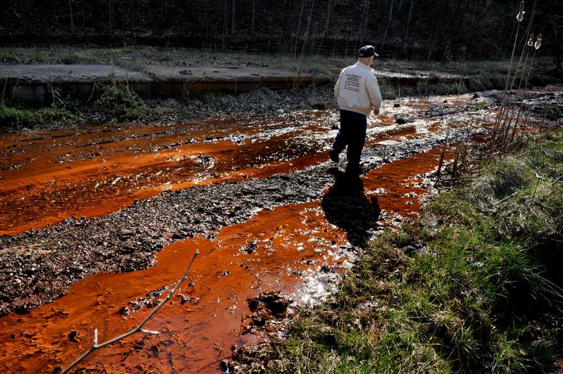 Larry Gibson (pictured) walks past leeching orange colored water (has sulfuric acid in it among other waste) that's flowing downhill near Kayford, West Va.