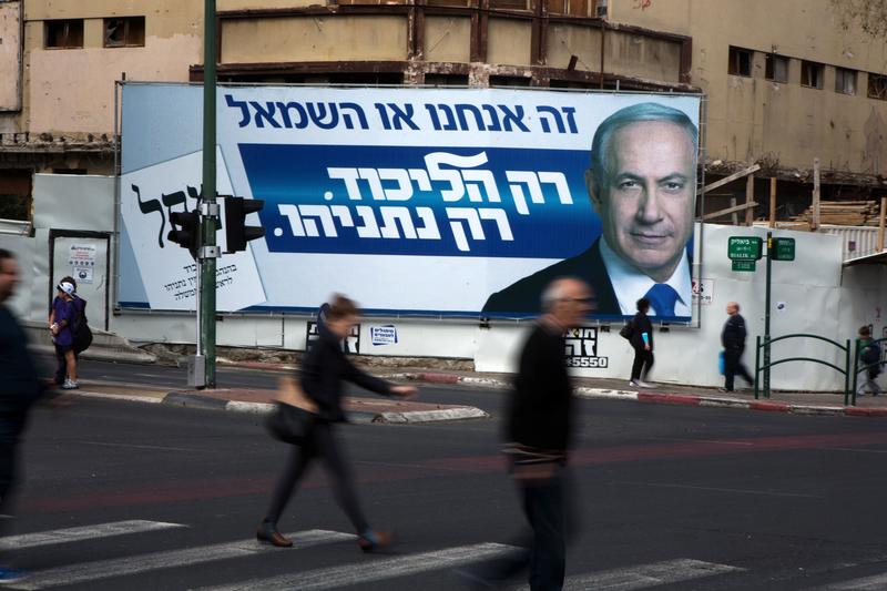 Israelis walk past by campaign posters showing Israeli Prime Minister and Likud party's candidate running for general elections, Benjamin Netanyahu on March 12, 2015.