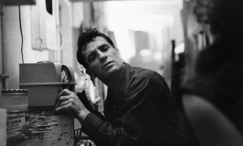 Jack Kerouac leans closer to a radio to hear himself on a broadcast, 1959