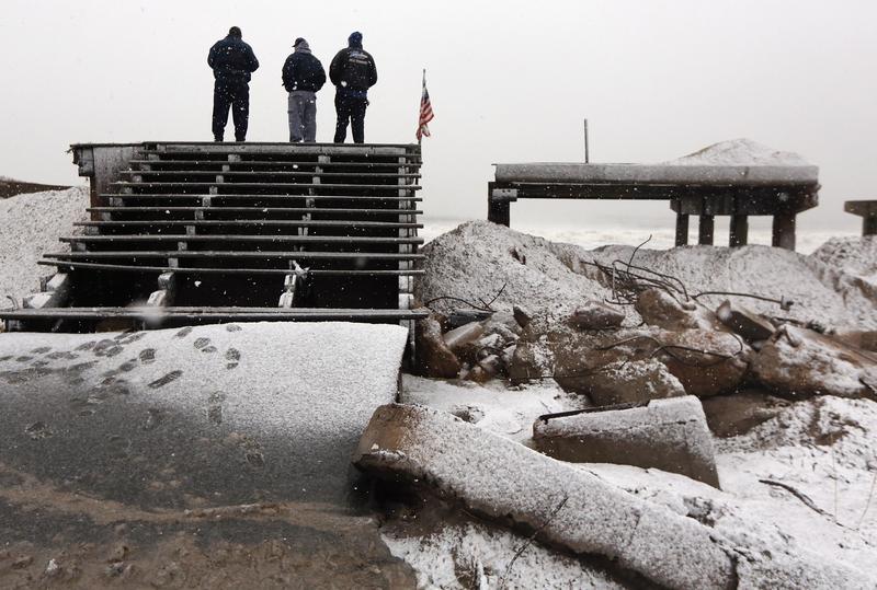 People stand on a destroyed section of boardwalk to check the storm's approach as a nor’easter arrives in New York City on November 7, 2012.