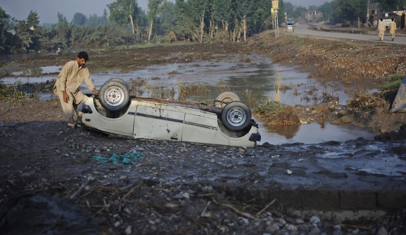 A Pakistani flood survivor inspects an overturned car in Charsadda on August 4, 2010. Devastating floods have swept away farmland and devastated livestock in Pakistan's northwest.