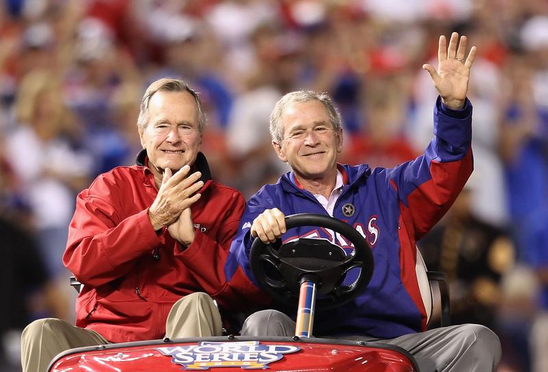 Former President George W. Bush and his father Former President George H.W. Bush wave to the crowd before a Texas Rangers World Series game in October 2010.