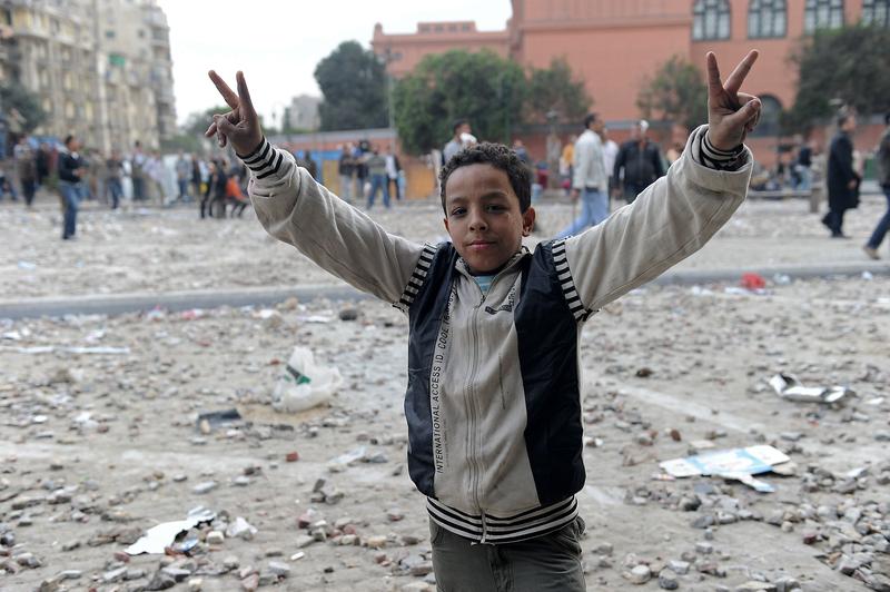 A young Egyptian anti-government demonstrator flashes victory signs as a stone battle rages between fellow demonstrators and pro-regime opponents at Cairo's Tahrir Square on February 3, 2011