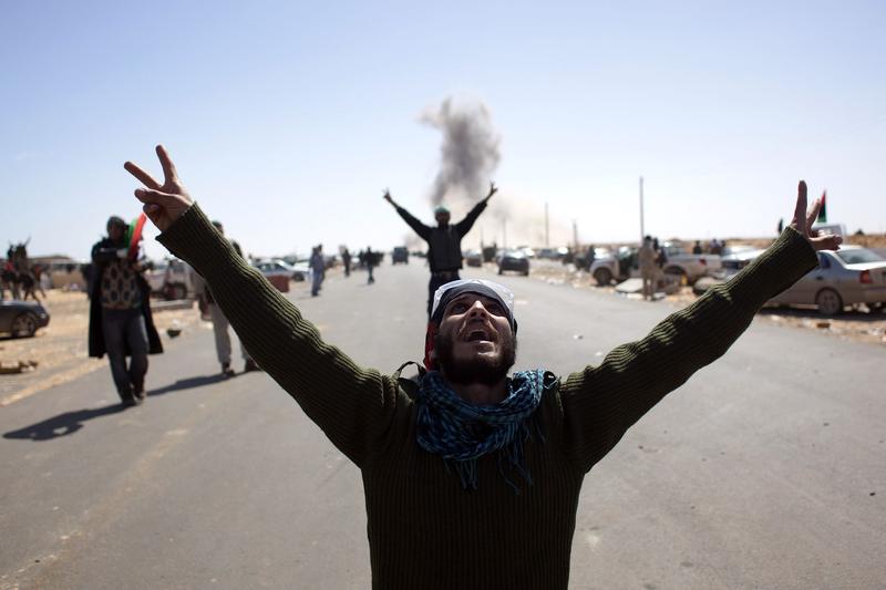 Libyan rebel fighters flash the victory sign as they look at an airforce fighter jet flying overhead after dropping a bomb near a checkpoint on the outskirts of the oil town of Ras Lanuf on March 7, 2