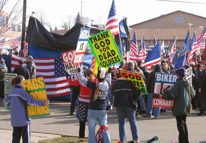 Members of the Kansas-based Westboro Baptist Church wave signs in front of a group of flag-waving bikers acting as human shields for a family holding a funeral for their son in Flushing, MI. (2006)