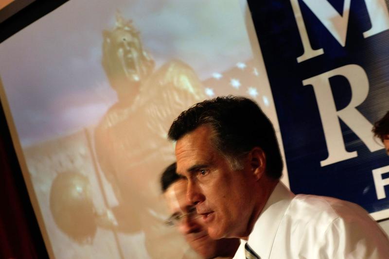 Republican presidential candidate and former Massachusetts Gov. Mitt Romney speaks to the media as a television ad plays behind him.