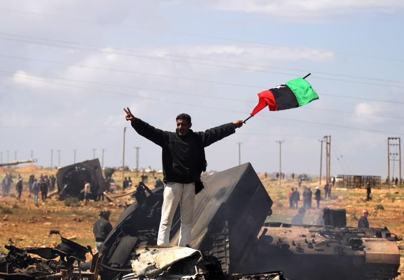 A Libyan rebel waves the rebellion flag as he stands over wrecked military vehicles belonging to Moammer Khaddafi forces hit by French warplanes on March 20, 2011.