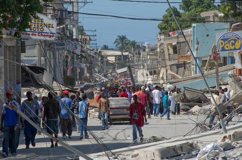 People wander the streets in front of the remains of a boarding school in the downtown area in Port-au-Prince, Haiti.