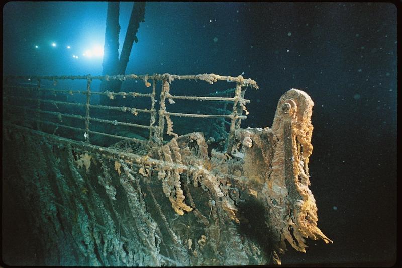 Bow railing of <em>R.M.S. Titanic</em> illuminated by Mir 1 submersible behind the forward anchor crane. Rustcicles' slant shows the direction of the current.