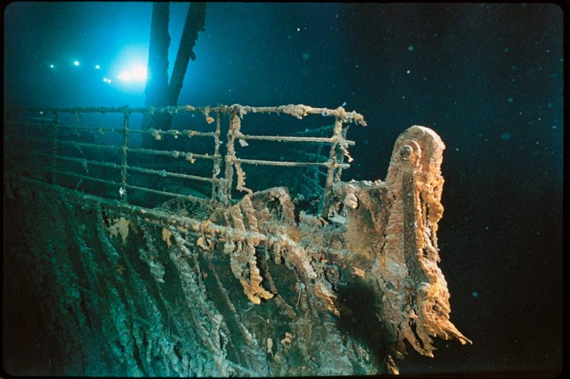 Bow railing of <em>R.M.S. Titanic</em> illuminated by Mir 1 submersible behind the forward anchor crane. Rustcicles' slant shows the direction of the current.
