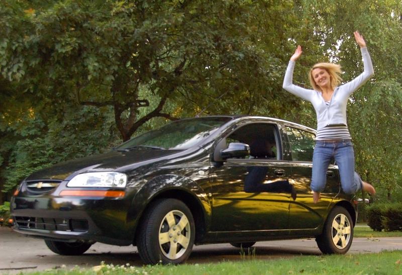 A woman jumping near her recently purchased car.