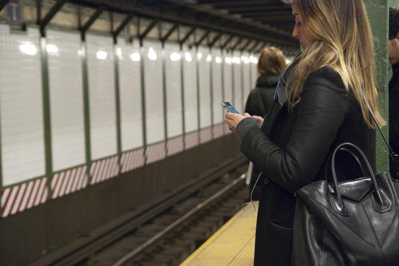 A woman uses her smartphone while waiting for the train in the Times Square subway station.
