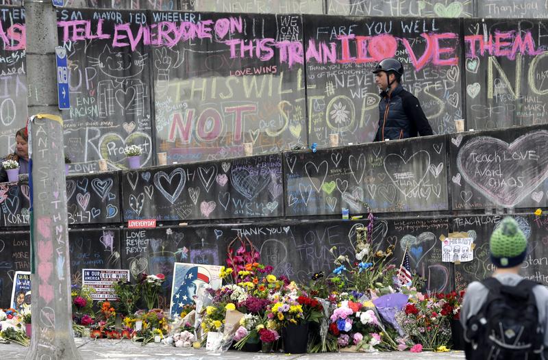 A bicyclist walking his bike down a ramp in Portland, Ore., Wednesday, May 30, 2017, is surrounded by messages, flowers, images and candles at the memorial for two men fatally stabbed on a light rail
