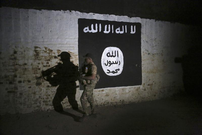 An Iraqi soldier inspects a recently-discovered train tunnel, adorned with an Islamic State group flag.