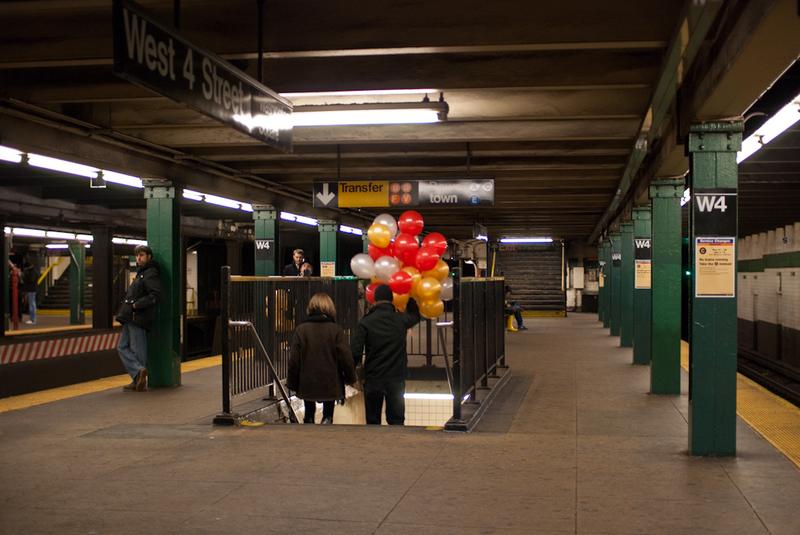 A couple holds hands, and balloons, on the NYC subway.