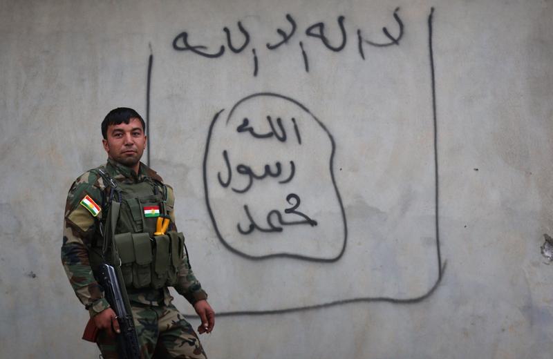 A Peshmerga fighter stands beside graffiti of the Islamic State (IS) group flag in Zummar city on December 18, 2014. Kurdish forces continue to battle IS fighters near Syria.