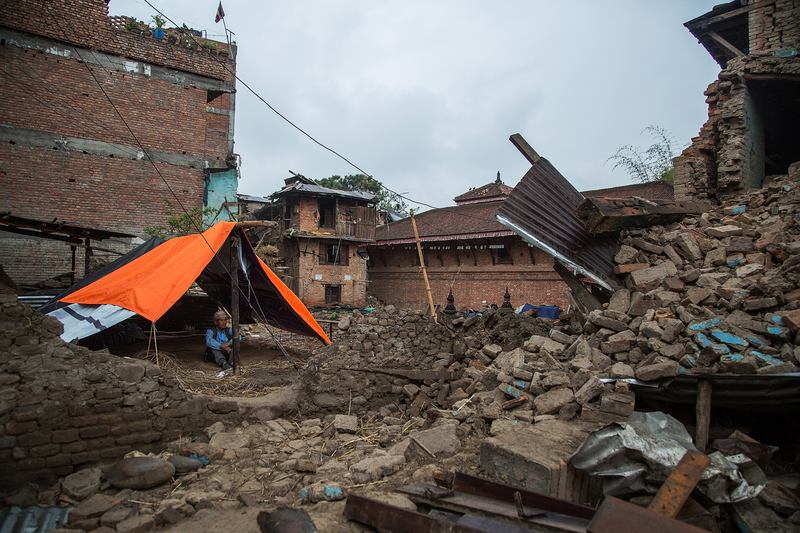A man sits underneath a tent set up in front of his collapsed home on April 30, 2015 in Bungamati, Nepal.