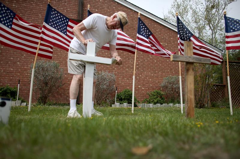 Bob Gordon paints a cross placed in front of 16 American flags as he helps build a memorial in front a church for the victims of the Fort Hood shooting on April 2, 2014.
