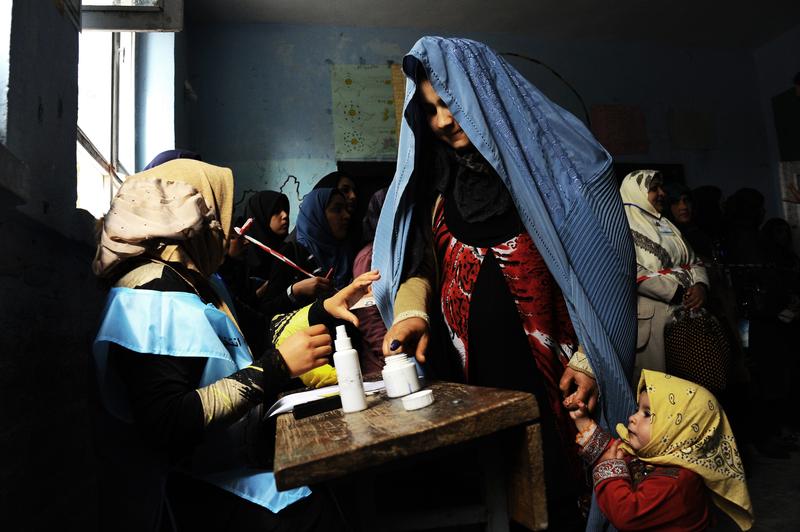 An Afghan woman (R) is guided by an official as she puts her finger in ink at a polling station in the northwestern city of Herat on April 5, 2014.