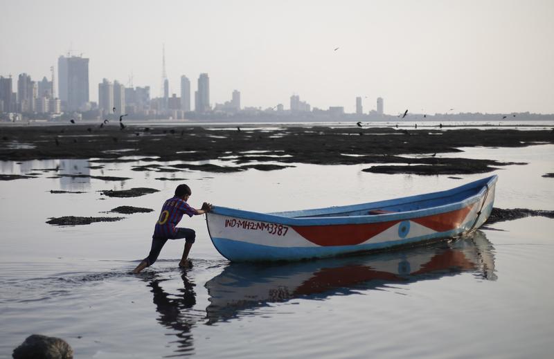 A boy pushes a boat as he plays near the shore of the Arabian Sea, in Mumbai, India, Sunday, Oct. 6, 2013.