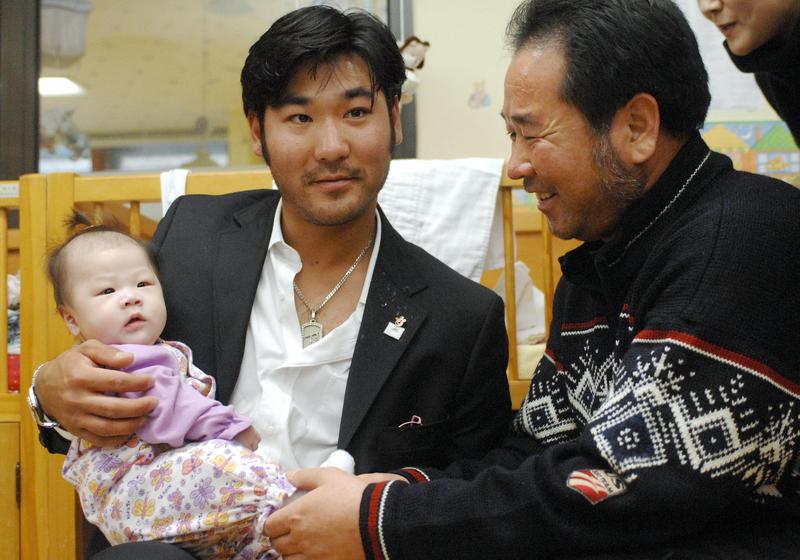 US Olympic skier Toby Dawson holds a baby in his arms as his South Korean father Kim Jae-Soo looks on while visiting a local adoption agency, Holt International Children's Service, in Seoul.