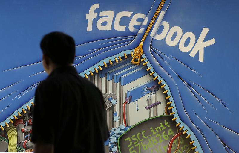 In this June 11, 2014 file photo, a man walks past a mural in an office on the Facebook campus in Menlo Park, Calif.
