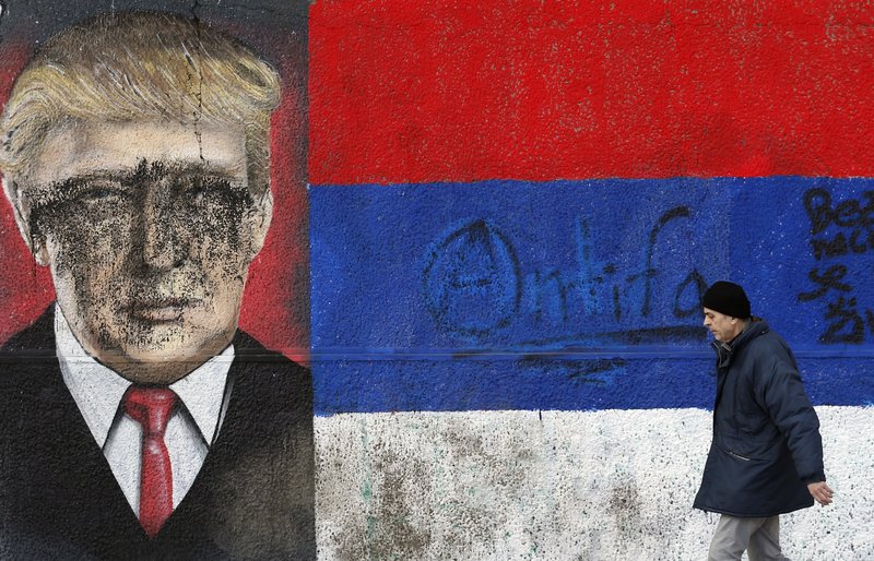 A man passes by graffiti depicting US President-elect Donald Trump vandalized with paint, in Belgrade, Serbia, Friday, Jan. 20, 2017.