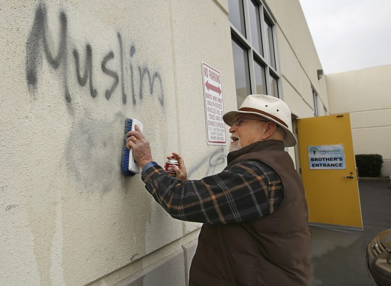 A man cleans racist graffiti off the wall of a mosque in Roseville, California.