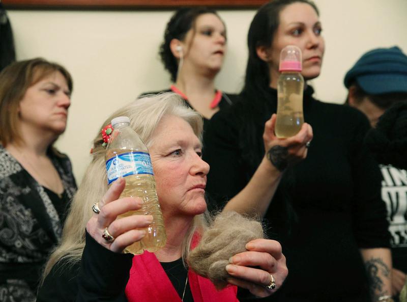Flint residents Gladyes Williamson (C) holds a bottle full of contaminated water, and a clump of her hair, alongside Jessica Owens, holding a baby bottle full of contaminated water. Feb. 16, 2016
