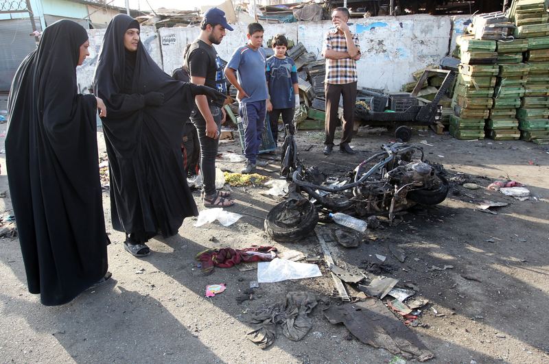 Iraqi onlookers gather on July 16, 2014 around a burnt motorcycle at the scene of an explosion that took place the previous night in Sadr City, one of Baghdad's northern Shiite-majority districts.