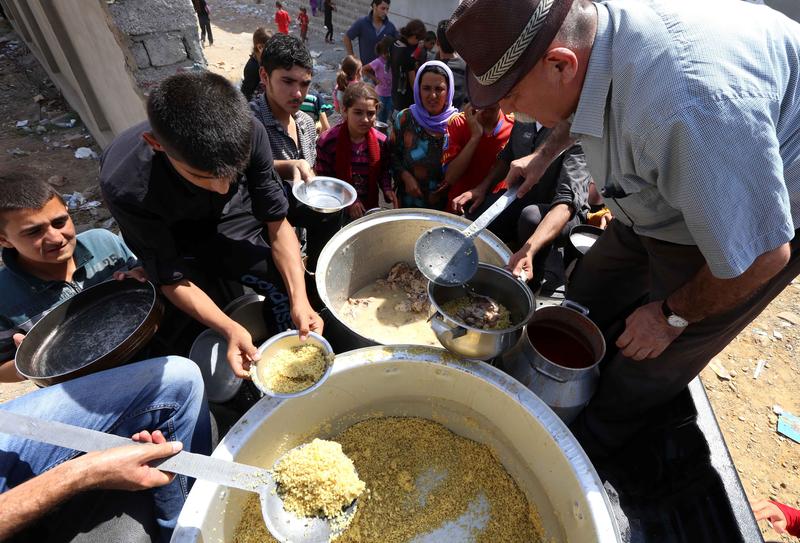Iraqi Yazidi families who fled the violence in the northern Iraqi town of Sinjar, are given food at a school where they are taking shelter in the Kurdish city of Dohuk