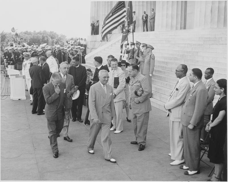 President Truman is leaving the podium area, accompanied by Walter White, President of the NAACP (to Mr. Truman's left) and Fred Vinson (between them). Gen. Harry Vaughan is to the right of Truman.